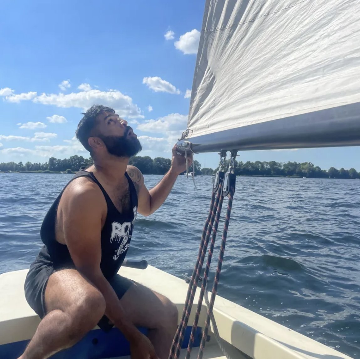 Vighnesh on a small sailboat on a lake, looking up at the sail