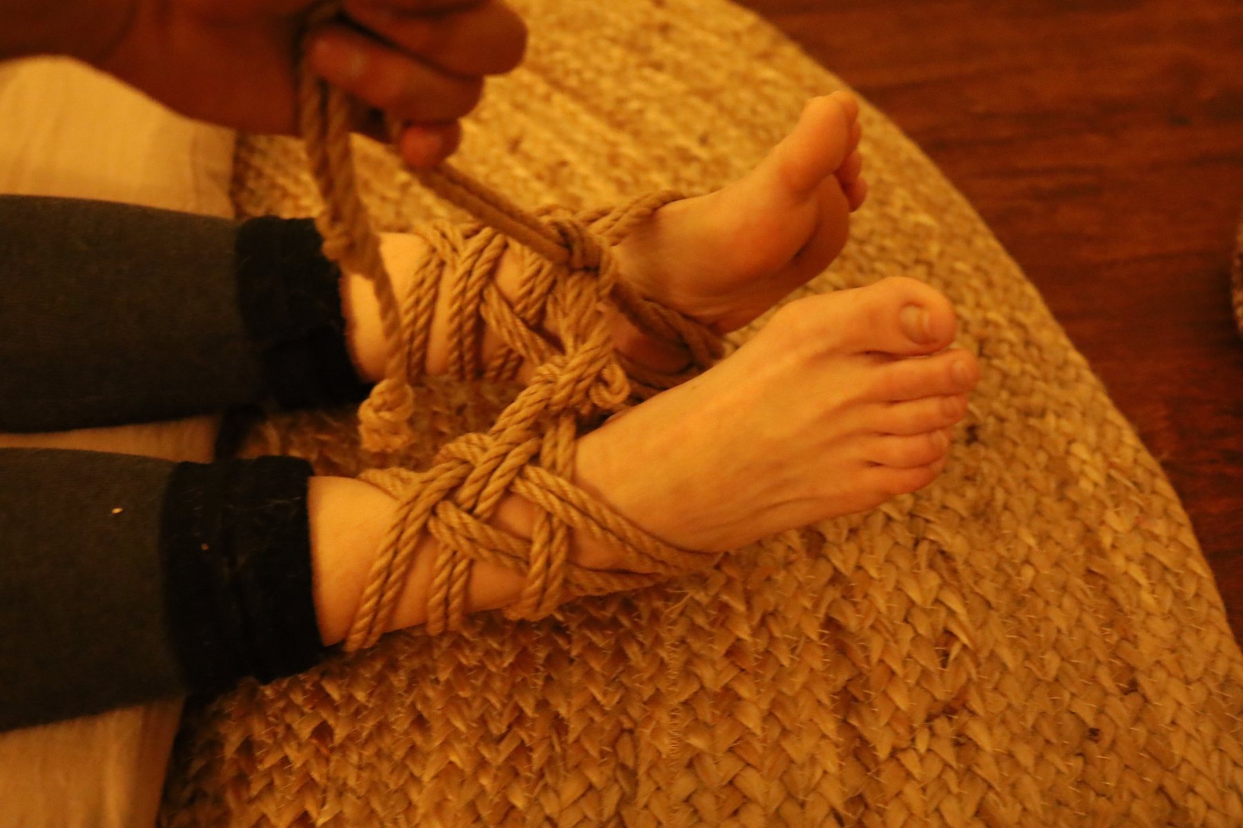 Ankles and feet bound in a woven rope tie on a jute rug